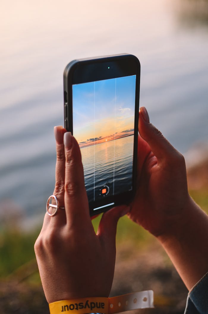 Woman records a stunning sunset over the sea using a smartphone.